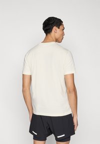 Κρεμ κοντομάνικη μπλούζα με στρογγυλή λαιμόκοψη, υφασμάτινη βαμβακερή υφή και απλό σχέδιο, συνδυασμένη με μαύρο σορτς με λευκές λεπτομέρειες.