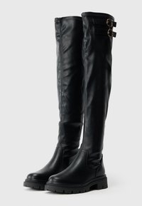 Μαύρες δερμάτινες μπότες πάνω από το γόνατο με λείο υφή, που διαθέτουν δύο διακοσμητικούς ιμάντες με χρυσές αγκράφες και παχύ, ανθεκτικό πάτο.