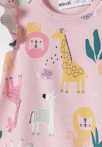 Camisa de algodón rosa con estampados de animales, que presenta una jirafa, una cebra y un león, acentuada con hojas verdes y colores juguetones. Detalle de hombro con volantes.