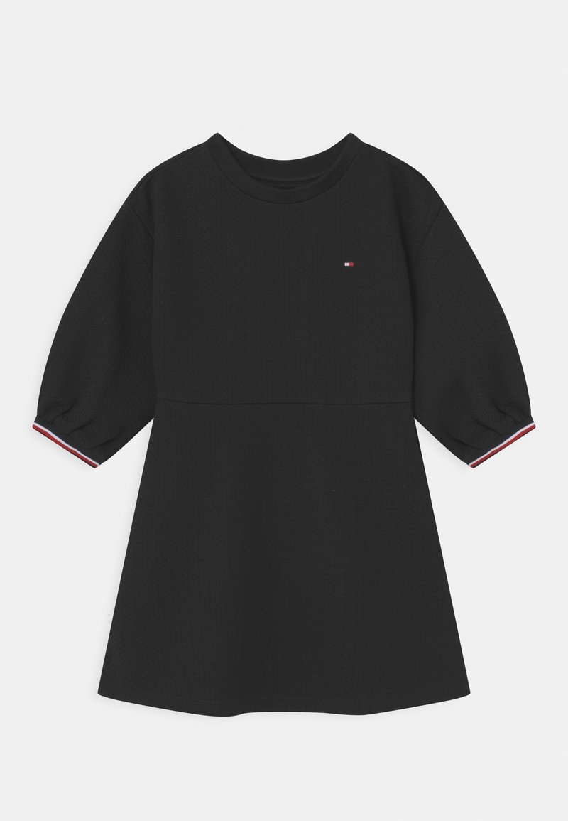 Czarna sukienka z teksturowanej tkaniny, okrągłym dekoltem i krótkimi bufkowymi rękawami. Ma małe logo oraz czerwono-białe wykończenie na rękawach.