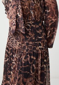 Braun und schwarz gemustertes Kleid aus transparenter Stoff, mit Rüscheärmel und einem taillierten Oberteil, das zu einem fließenden, gerafften Rock führt.