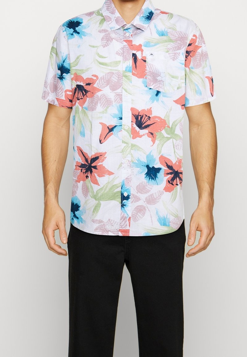 Lyhythihainen paita kevyestä kankaasta, jossa on kukkakuosi vaaleanpunaisen, sinisen ja vihreän sävyissä; nappikaulus ja tasku vasemmalla.