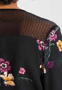 Mustapaita, jossa on kukkakuvio purple, keltaisen ja vihreän sävyissä, ja jossa on pilkullinen verkko-osa hartioilla ja lyhyet hihat. Pehmeä kangas.