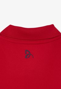 Röd polo tröja med strukturerad tyg och ribbad krage. Har en mörk logotyp på ryggen strax under kragen.