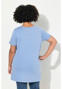 Camiseta de manga corta azul claro con cuello redondo, que presenta un corte holgado y un suave tejido de algodón, extendiéndose hasta la cadera.