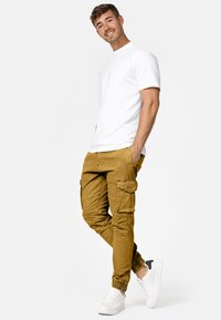 Pantalones cargo en color caqui con múltiples bolsillos, con puños estrechos y cinturilla elástica. Combinados con una camiseta blanca lisa y zapatillas blancas.