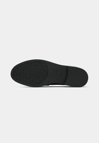Semelle de chaussure noire avec motif de grip texturé, présentant une forme arrondie et des bords lisses. Fabriquée en caoutchouc durable.