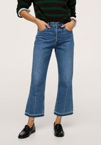 Jean flare en denim avec taille haute, ourlet brut, couleur bleu clair et discrètes décolorations, associé à des mocassins noirs.