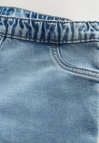 Shorts en denim bleu clair avec une taille élastique froncée, des détails de couture visibles et une petite poche avant. Texture lisse dans l'ensemble.
