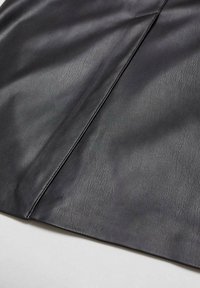 Tissu en cuir noir lisse avec une couture visible en diagonale, montrant la texture et de légères rides sur une surface plane.