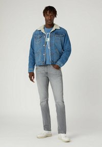 Chaqueta de mezclilla con cuello de borreguito, color azul, con cierre de botones y dos bolsillos en el pecho, combinada con jeans grises y zapatillas blancas.