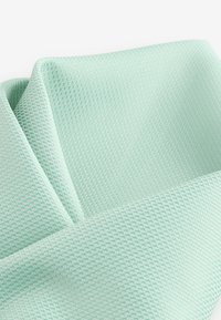 Lys grøn tekstureret stof med et mesh-mønster, der viser glat og fleksibelt materiale, foldet med en blød, let skinnende overflade.