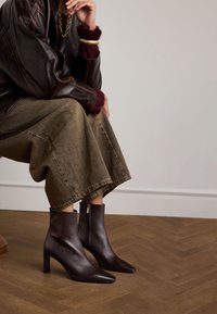 Dunkelbraune Lederan ankle boots mit spitzen Zehen und Blockabsätzen. Seitlicher Reißverschluss. Getragen mit einem grünen Rock und einer braunen Lederjacke.
