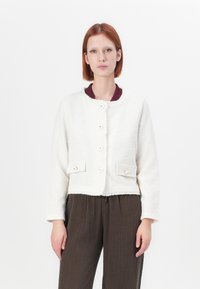 Veste cropped blanche en tissu texturé, avec un col rond, cinq boutons et deux poches avant à fermeture à bouton.