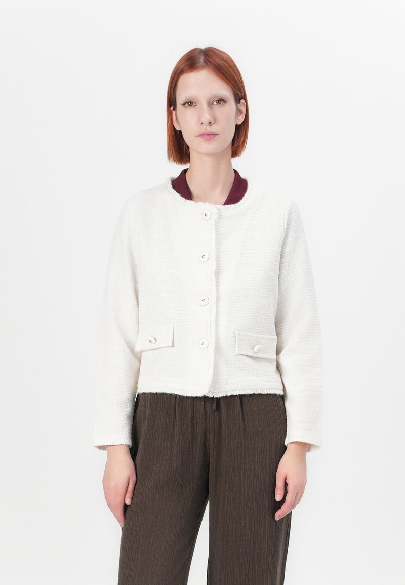 Veste cropped blanche en tissu texturé, avec un col rond, cinq boutons et deux poches avant à fermeture à bouton.