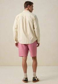 Chemise légère jaune clair à boutons, avec des rayures verticales, associée à un short rose texturé. Baskets avec des accents verts et blancs.