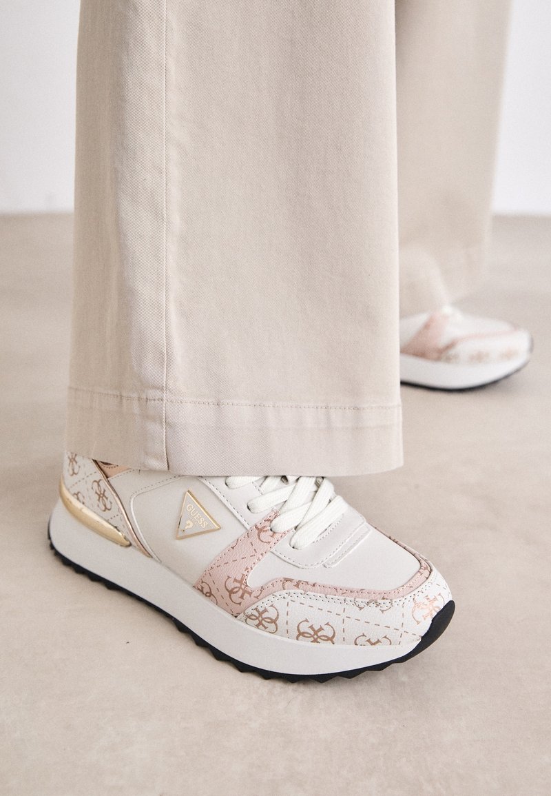 Valkoiset lenkkarit, joissa on vaaleanpunainen ja kultainen kuvio, metalliset yksityiskohdat ja teksturoitu pito. Mukana nauhat ja kolmiomainen logo sivussa.