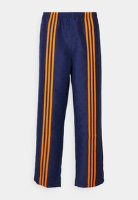 Marineblå bukser med et helhetlig mønster, med tre tydelige oransje striper som går ned langs hver side. Elastisk midjebånd øverst.