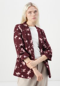 Blazer floreale bordeaux realizzato in un tessuto leggero, con motivi di fiori rosa e verdi, apertura frontale e maniche a tre quarti.