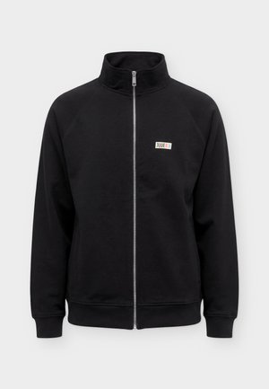 Veste noire à manches longues zippée avec col haut et petit écusson rectangulaire avec le logo sur la poitrine gauche indiquant « Juve » avec des bandes colorées.