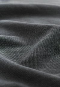 Tissu gris foncé avec un tissage fin et texturé, affichant des plis doux et un éclat subtil. Le matériau semble flexible et lisse.
