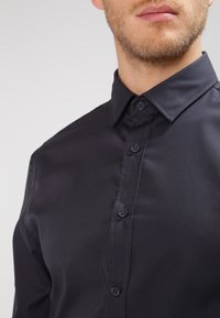 Dark blue button-up shirt with a smooth texture, featuring a classic collar and six buttons along the front placket.