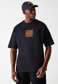T-shirt nera a maniche corte con una grafica arancione "NEW ERA" sul davanti. Abbinata a un cappellino blu, completa un look casual.