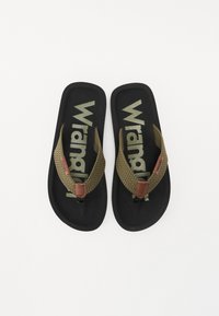 Tongs noires avec des sangles tissées vert olive et des accents en cuir marron. Leur semelle arbore le logo "Wrangler" dans une couleur contrastante.