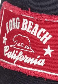 Red fabric patch with frayed edges, featuring white embroidered text "LONG BEACH" and "California," and a bear graphic with stars.