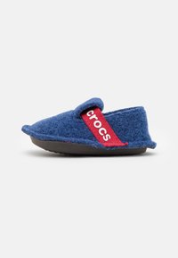 Scarpa blu in feltro senza lacci con suola in gomma nera, caratterizzata da una cintura di tessuto rosso con il logo "crocs". Forma arrotondata e superficie testurizzata.