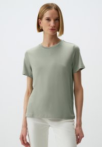 T-shirt in cotone verde chiaro con scollatura tondeggiante, maniche corte e texture liscia. Presenta un delicato dettaglio di cucitura lungo le spalle.