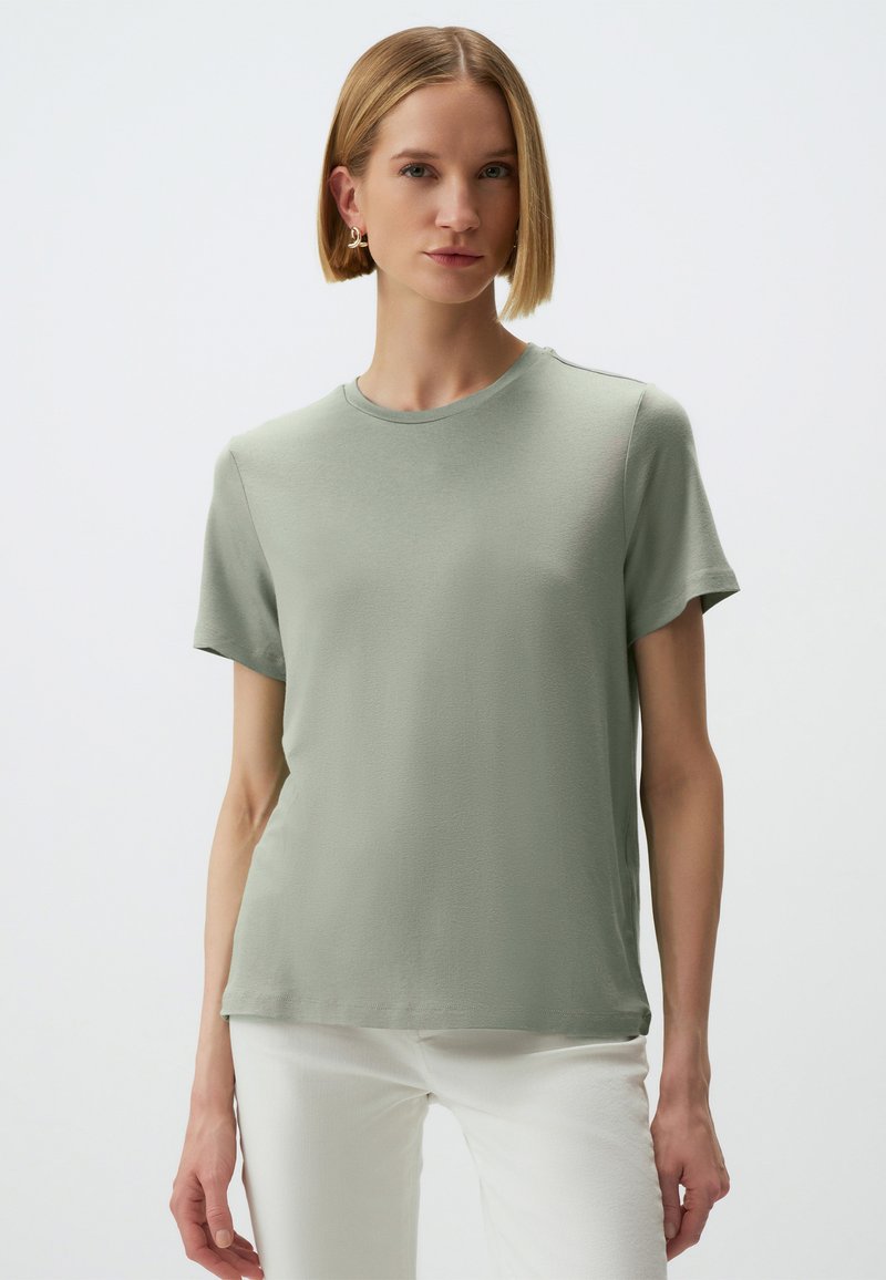 T-shirt in cotone verde chiaro con scollatura tondeggiante, maniche corte e texture liscia. Presenta un delicato dettaglio di cucitura lungo le spalle.