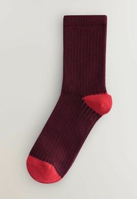 Burgundy sock with ribbed texture, featuring a bright red heel and toe. Mid-calf length, seamless construction. Smooth fabric.