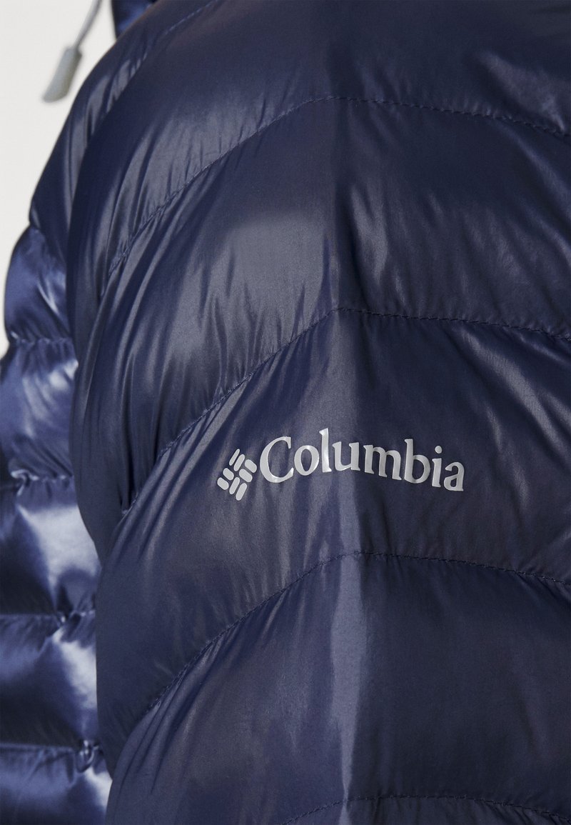Veste matelassée marine avec une finition brillante, présentant un design matelassé et un logo "Columbia" argenté sur le côté gauche.