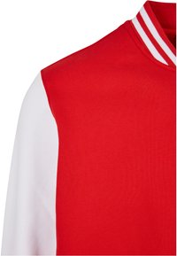 Rød treningsjakke med en glatt tekstur, som har hvite ermer og en stripete krage. Designet fremhever sporty estetikk.