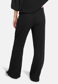 Zwarte, geribbelde wijde broek met een relaxte pasvorm. Zachte stof, hoge tailleband en zijsplitten aan de zoom. Geschikt voor casual wear.
