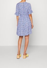 Blommig klänning i ljusblått med korta volangärmar, midja som är insvängd och en utsvängd kjol. Bärs med gula träskor och träklackar.