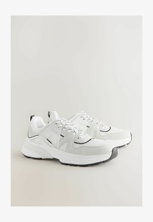 Scarpe da ginnastica bianche realizzate in materiali mesh e suede, con dettagli neri, lacci testurizzati e una suola bianca spessa con un cappuccio grigio sulla punta.