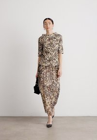 Robe imprimée léopard à manches courtes, avec une texture lisse et une silhouette fluide, complétée par des accessoires et des talons noirs.