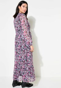 Robe maxi en tissu transparent, présentant un motif floral multicolore avec une dominance de rose et de bleu. Manches longues, ourlet volants, associée à des bottes noires.