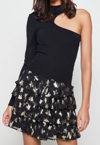 Svart enaxlad topp med ribbad textur, kombinerad med en lager-på-lager mini kjol med guldstjärnmönster på svart bakgrund.