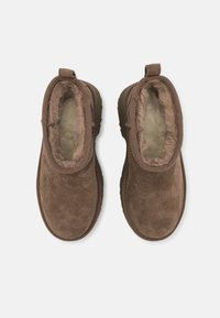 Paire de chaussures marron en daim à enfiler avec doublure en fourrure moelleuse, vue de dessus sur fond blanc.