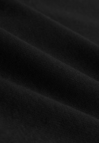 Juoda medžiaga su lygiu paviršiumi, kurioje matyti subtilūs įstrižainės formos ribai ir švelnūs raukšlėjimai, pabrėžiantys vienodą spalvą ir raštą.