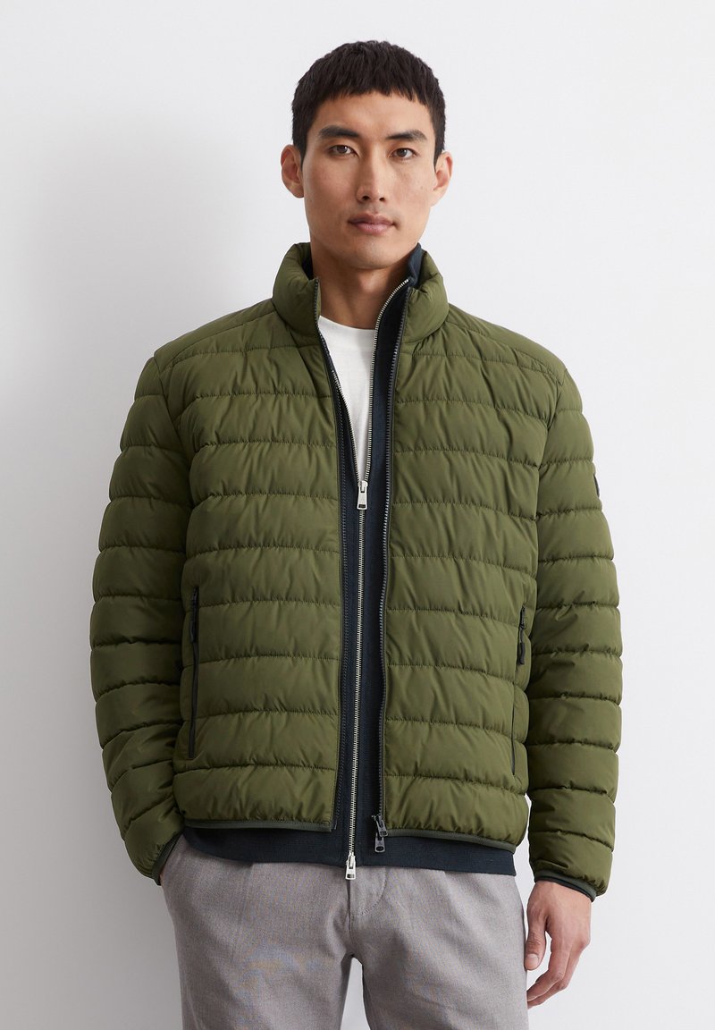 Olive green puffer jacket featuring a high collar, horizontal quilted pattern, and contrasting navy zipper. Two side pockets included.