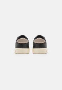 Zapatillas de cuero negro con suelas de goma beige. Parte trasera redondeada con un suave acento beige en el talón. Diseño minimalista, sin marcas visibles.