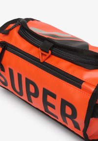 Oranje waterdichte tas met een getextureerd oppervlak, voorzien van een zwarte rits, zwarte accenten en grote zwarte tekst met de tekst "SUPER." Driehoekige ritstrekkker.