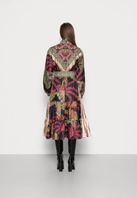 Abito con motivo floreale in colori vivaci, caratterizzato da maniche lunghe, orlo a balze a più strati e un accento dorato lucido in contrasto sulle maniche.