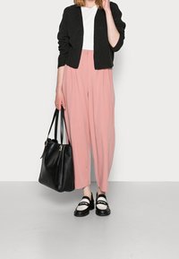 Cardigan nero lavorato a maglia, t-shirt bianca, pantaloni plissettati rosa, borsa nera con dettagli dorati e scarpe bianche e nere con cinturini.
