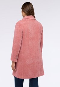 Hellrosa Mantel aus strukturiertem Stoff mit Schalkragen, langen Ärmeln und Knopfdetails an den Manschetten. Modell von hinten betrachtet.