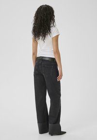 Black denim jeans with a wide leg shape, cuffed hems, and back pockets. Paired with a fitted white t-shirt and a black belt.